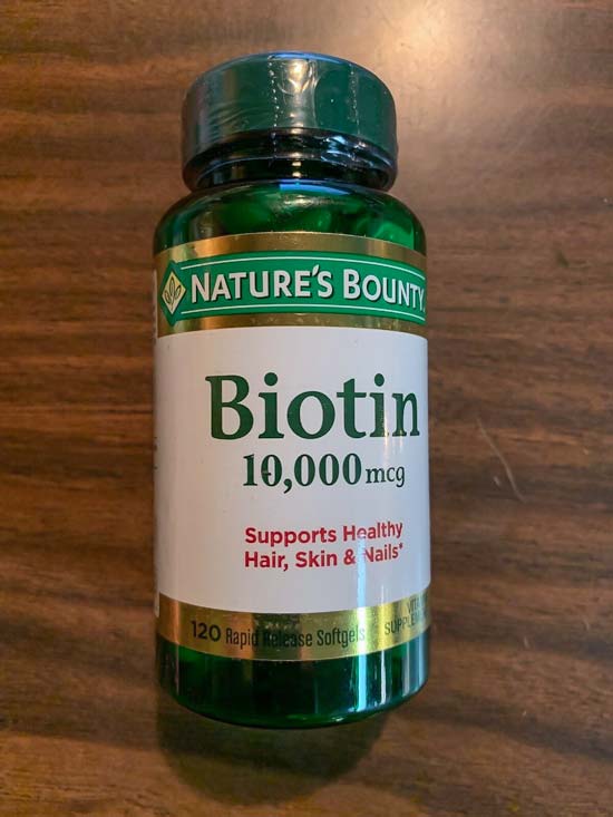 Image of a bottle of Nature's Bounty 10,000 mcg Biotin on a dark brown wood table